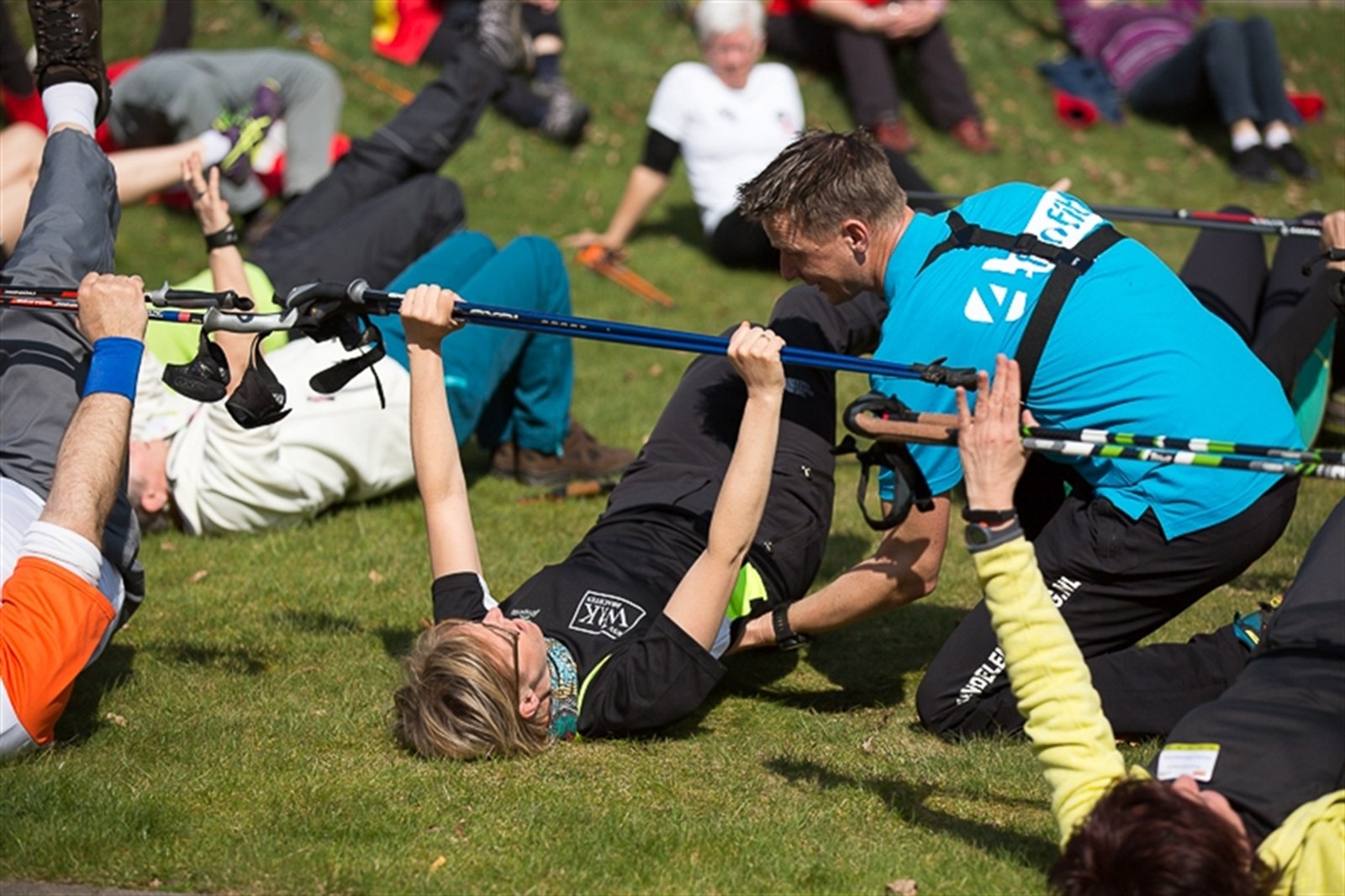 Deelnemers doen buikspieroefeningen met Nordic Walking-stokken op het gras tijdens een 4 Fun Fit training